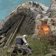A fantasy warrior kneels dejectedly at the corpse of a dragon.